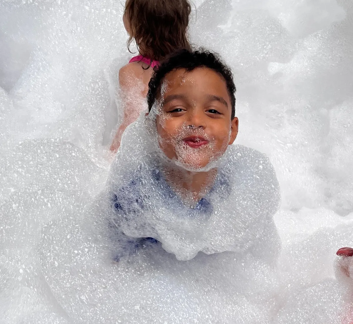 A child grinning from a mountain of foam at a foam party