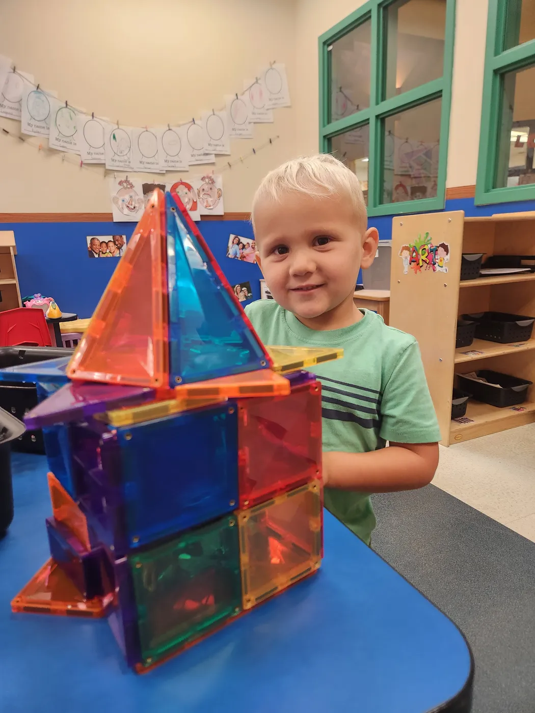 A preschooler smiling behind a tower of colorful magnetic tiles