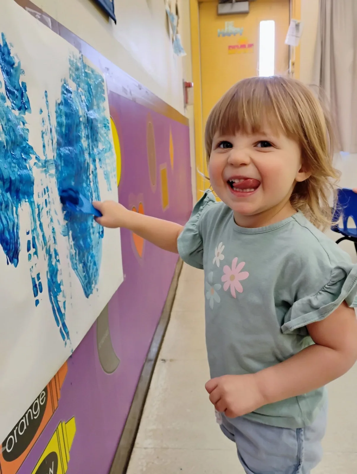 A child smiling beside a blue handprint painting at Northland